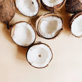 Halbierte Kokosnüsse mit weißem Fruchtfleisch und braunen Schalen auf hellbeiger Oberfläche inspirieren Thats me Organic® festes Shampoo - ideal für empfindliches Haar.