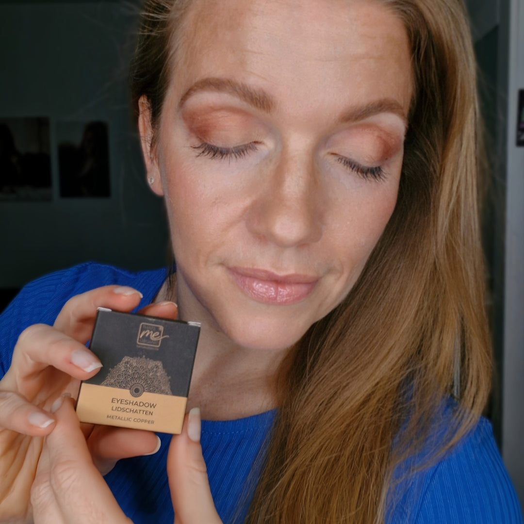 Frau mit geschlossenen Augen trägt pfirsichfarbenen Lidschatten und hält eine Dose mit der Aufschrift Eyeshadow Metallic Copper-Thats me Organic® Naturkosmetik Lidschatten ist titandioxidfrei und verleiht einen strahlenden Look.