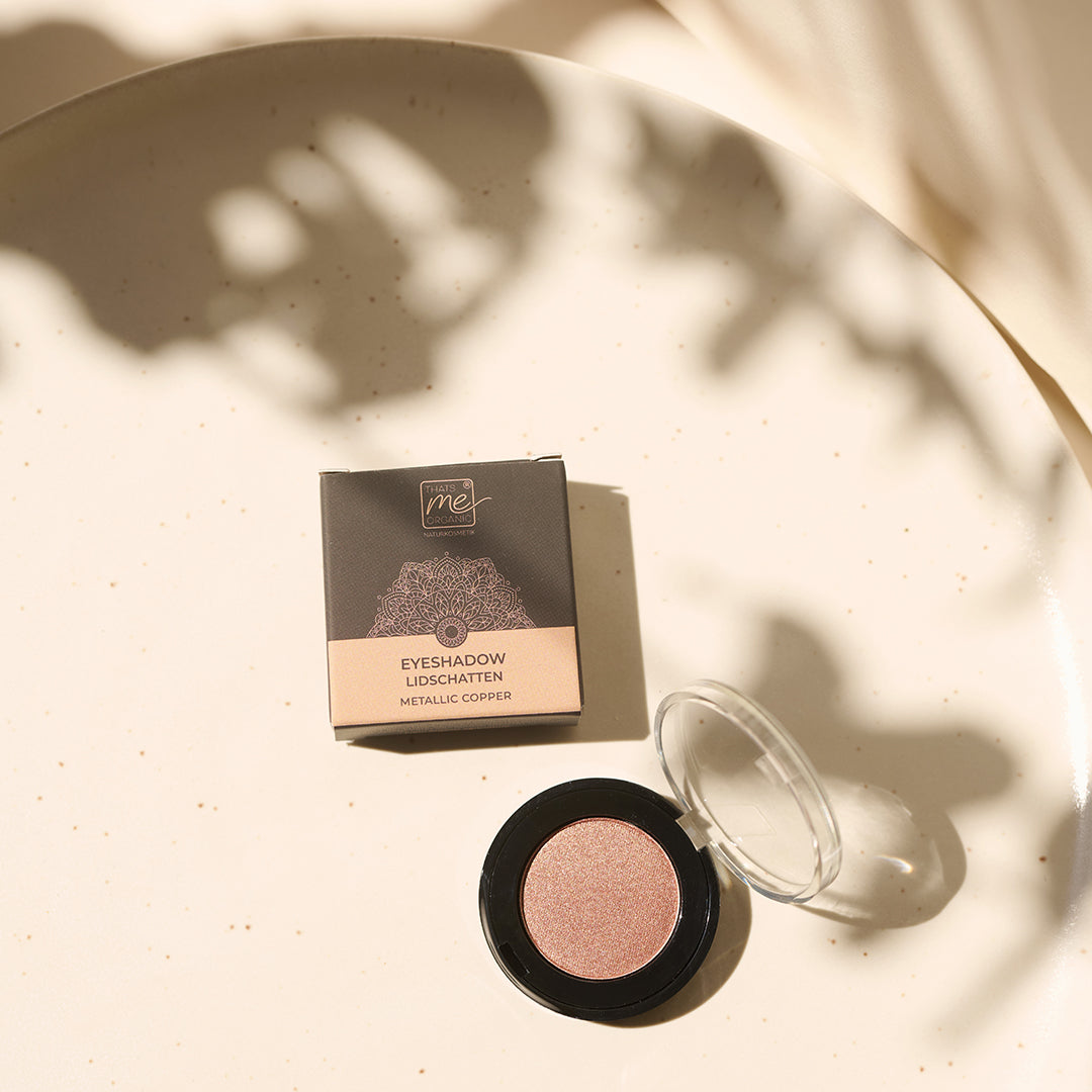 Thats me Organic® titandioxidfreier Naturkosmetik Lidschatten in Metallic Copper mit Verpackung, präsentiert auf heller, gesprenkelter Oberfläche im weichen Sonnenlicht.