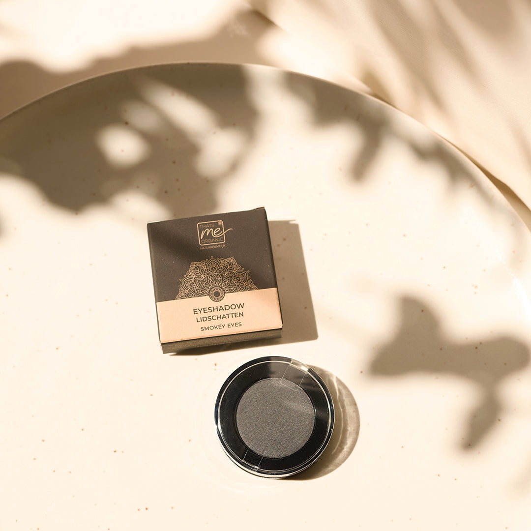 Single black Thats me Organic® Naturkosmetik Lidschatten und seine Verpackung auf cremefarbenem Untergrund mit weichen Schatten und Sonnenlicht.